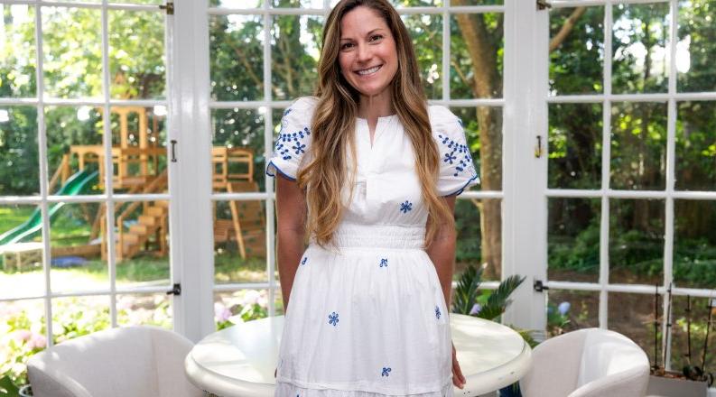 A woman in a white dress leans in a table in a room 